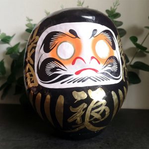 Black Japanese daruma doll that is 15cm tall with gold details