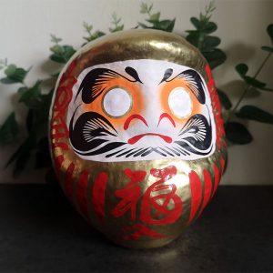 Black Japanese daruma doll that is 15cm tall with gold details