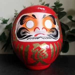 Red Japanese daruma doll that is 15cm tall with gold details
